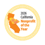 A circular emblem with a yellow decorative border contains an orange silhouette of California with a yellow and orange flower petal on top. Text within the emblem reads "2026 California Nonprofit of the Year".