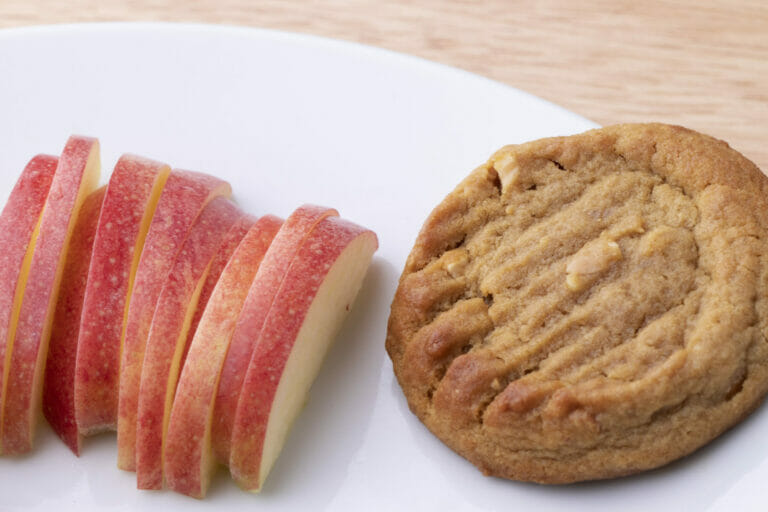 Close-up of a peanut butter cookie and apple slices on a white plate.