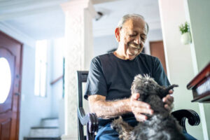 An elderly man with a mustache smiles as he holds a small, scruffy dog in his lap while sitting in a rocking chair.