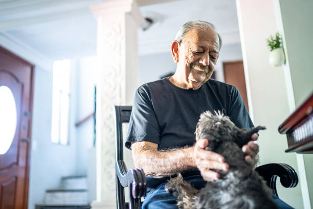 An elderly man with a mustache smiles as he holds a small, scruffy dog in his lap while sitting in a rocking chair.
